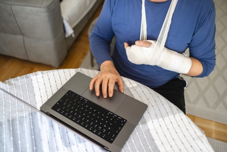 man, using a laptop while having a hand in the orthopedic cast